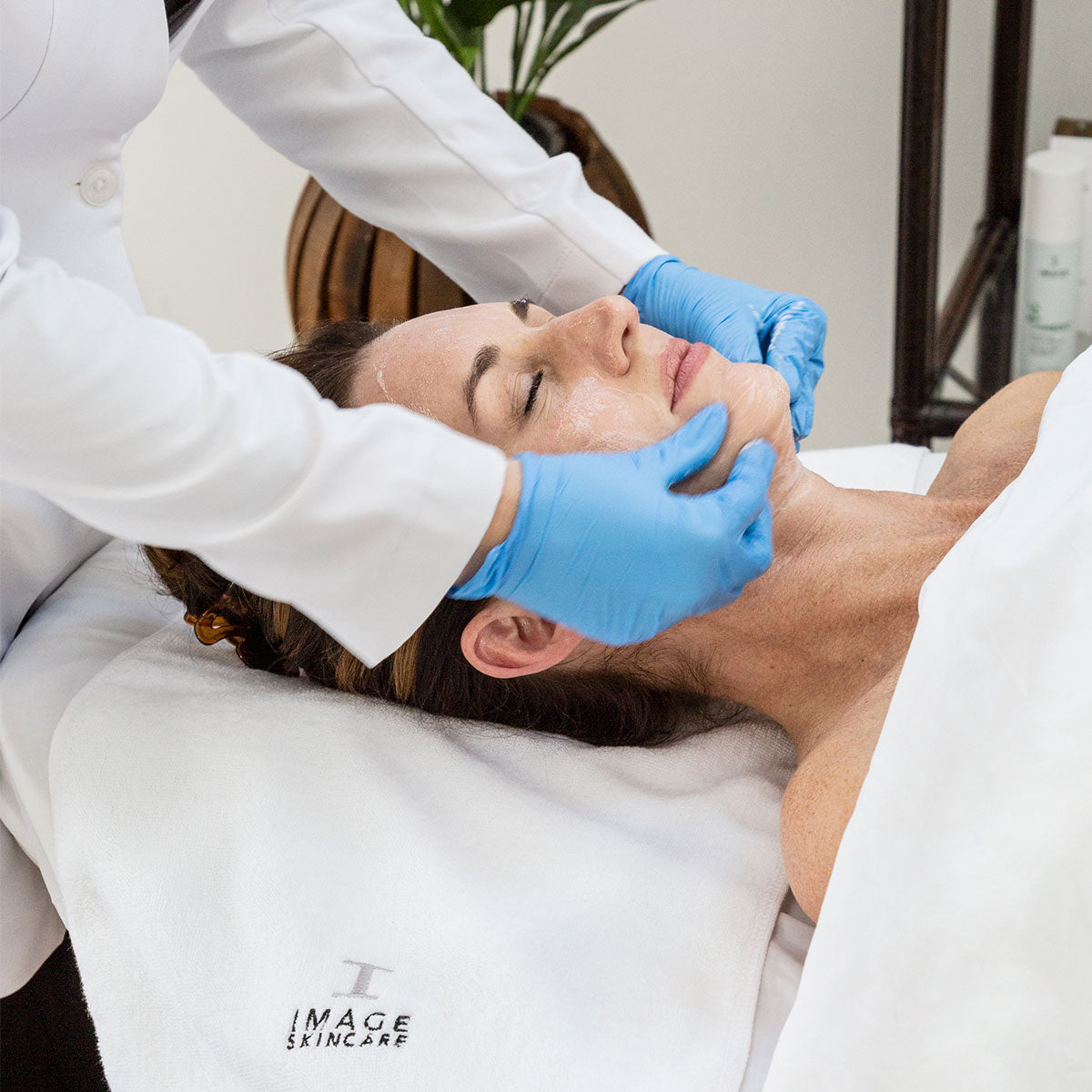 Person receiving a facial massage with gloved hands gently pressing on their cheeks and jawline.